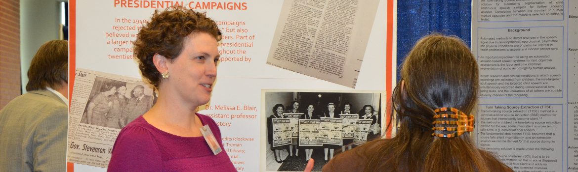 two women discussing research displayed at booth