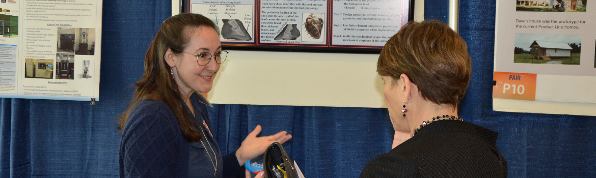 two women discussing research displayed at symposium booth