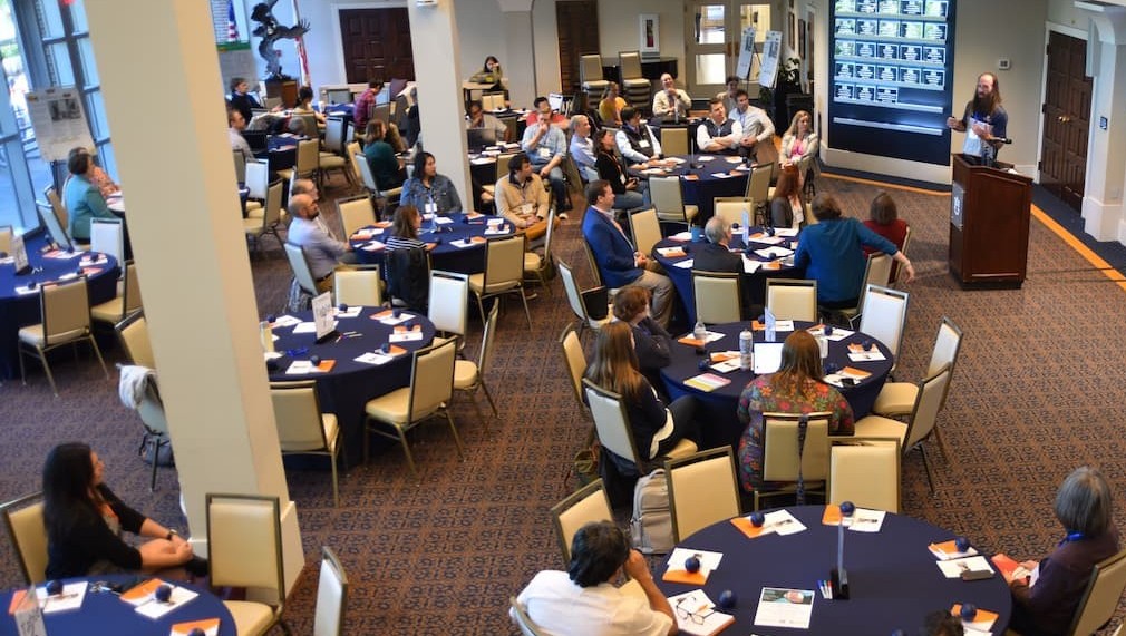 overhead view of a room of full tables and a speaker
